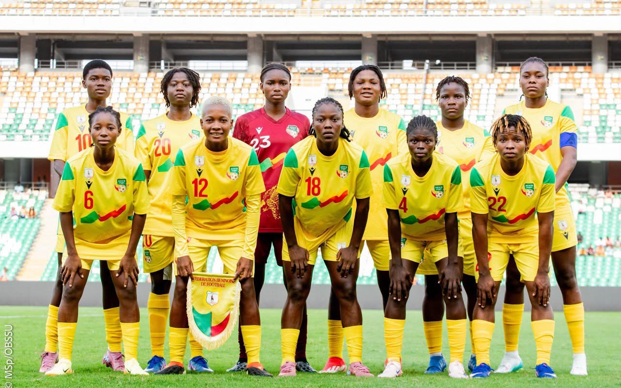 Onze joueuses en tenue jaune posent en rang devant les gradins d’un stade de football vide