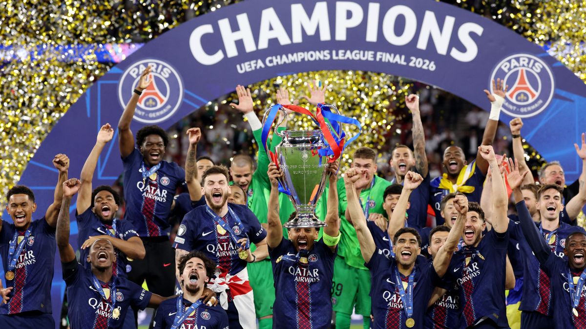 Des joueurs de football en maillot bleu foncé célèbrent une victoire en levant un trophée sous un arc "Champions UEFA Champions League Final 2026