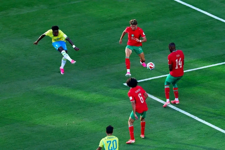 Un joueur en jaune tire le ballon au pied devant quatre joueurs en rouge sur le terrain de football
