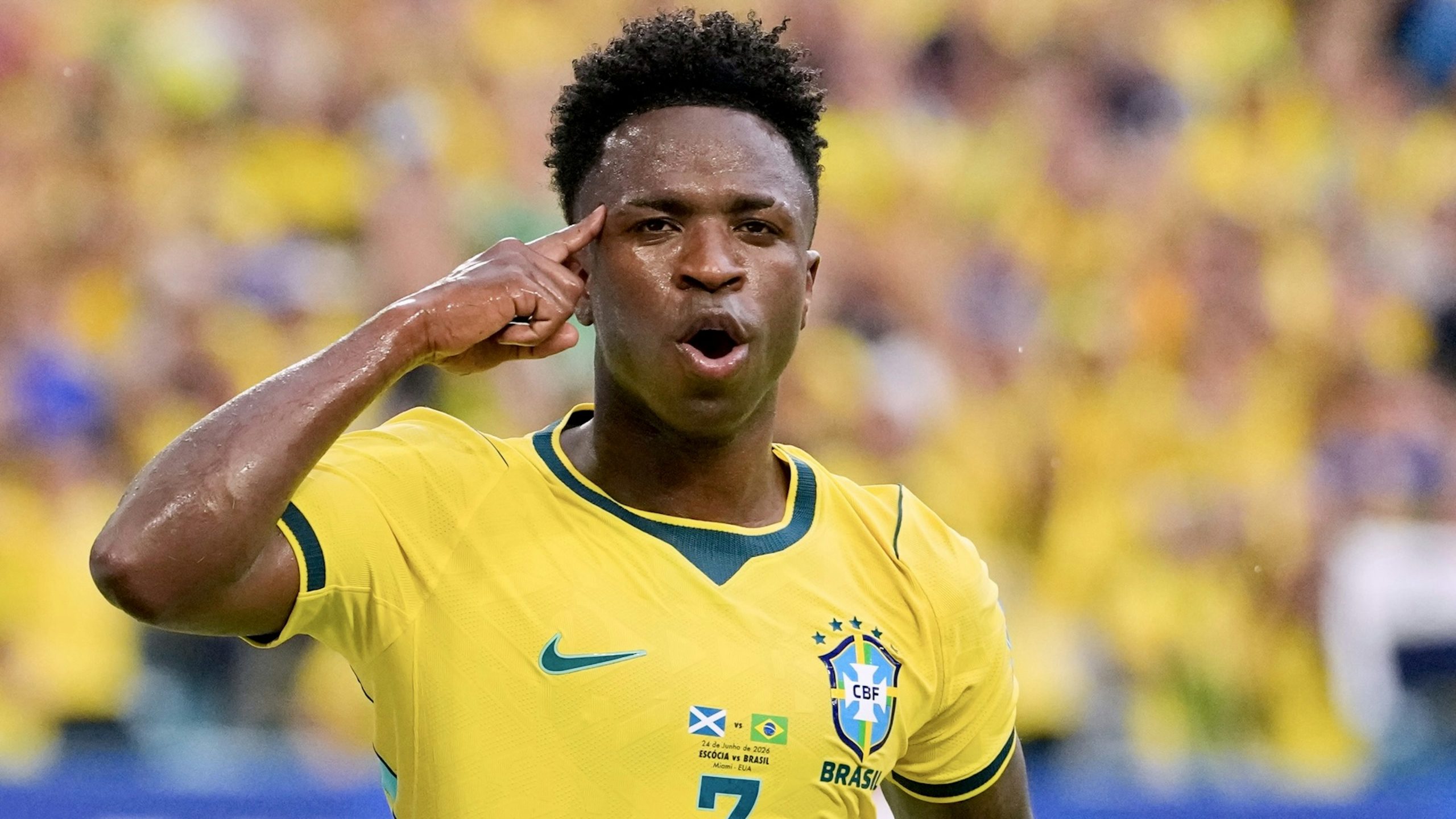 Un joueur de football en maillot jaune marque un but et célèbre en pointant sa tête avec son doigt devant un public flou en arrière-plan