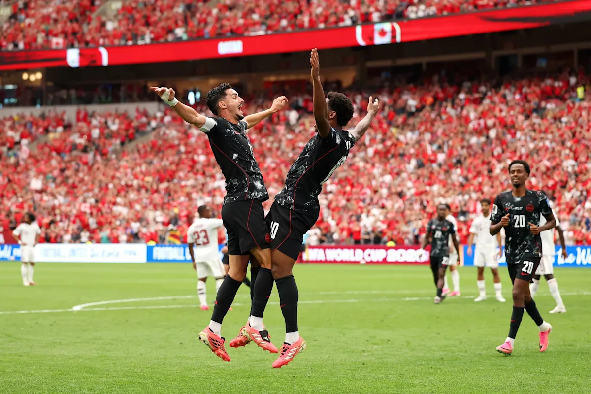Deux joueurs en maillots noirs sautent pour célébrer un but devant des spectateurs en tribunes rouges