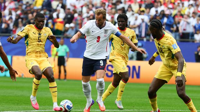 Un joueur en maillot blanc entouré de trois joueurs en maillot jaune tentant de contrôler un ballon sur un terrain de football