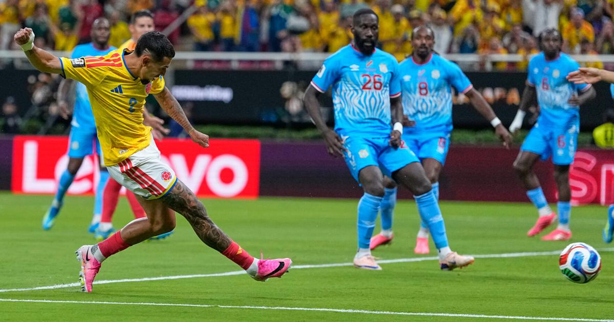 Un joueur en maillot jaune tire au but tandis que plusieurs joueurs en bleu tentent de défendre sur un terrain de football.