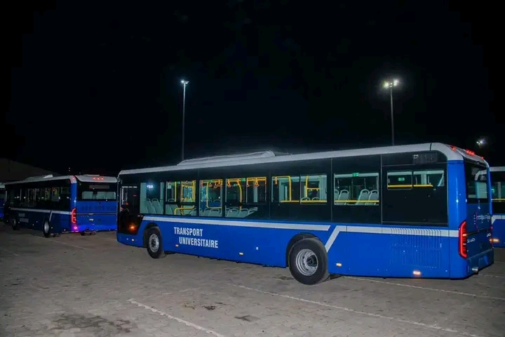 Deux bus bleus immobiles sur un parking éclairé la nuit avec l'inscription "TRANSPORT UNIVERSITAIRE" sur le côté