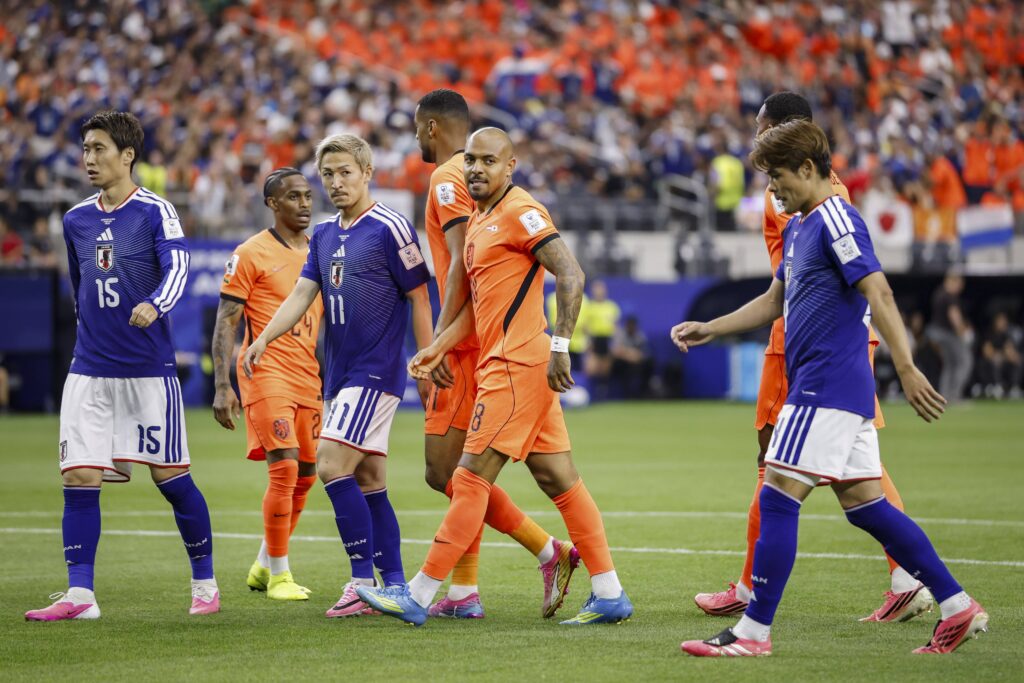 Des joueurs de football en maillots bleu et orange se croisent sur le terrain lors d’un match sous une foule dans un stade