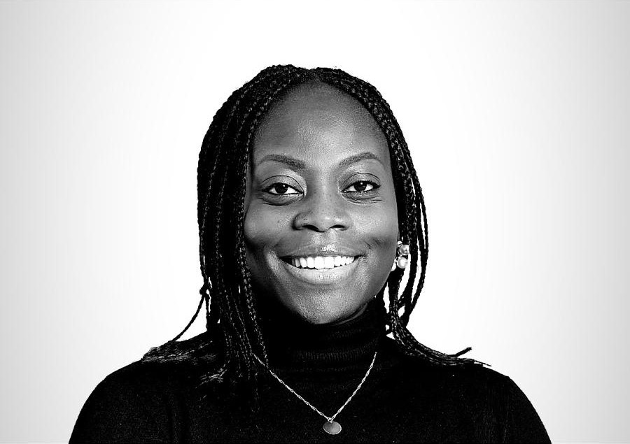 Portrait en noir et blanc d’une femme souriante avec des tresses portant un pull noir et un pendentif rond