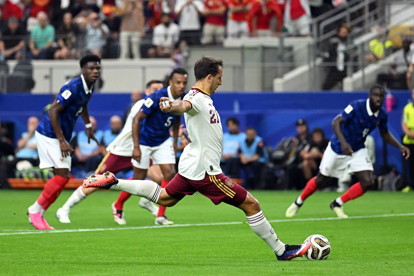 Joueur en maillot clair tirant un penalty face à des adversaires en maillot bleu sur un terrain de football